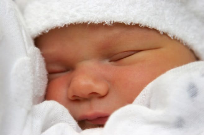A newborn baby snuggling into white linen